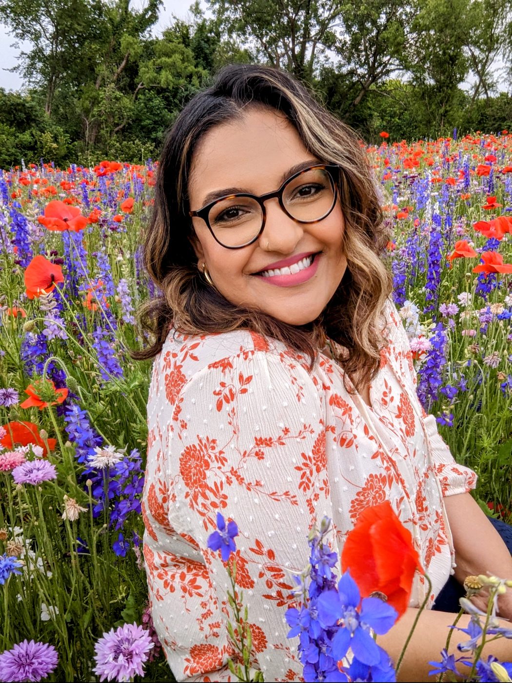 Ashmi smiling warmly in a field of red and purple wildflowers